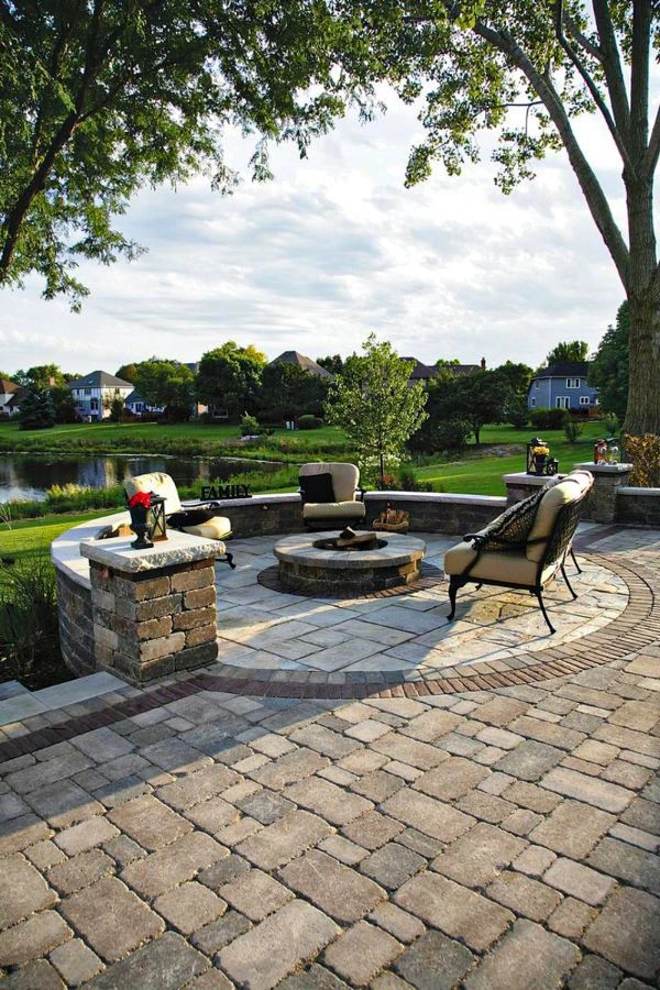 Lakefront concrete patio in Lewisville TX with stone pillars, decorative paver patterns, and built-in fire pit offering stunning water views and comfortable seating areas.