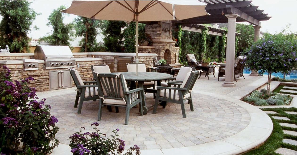 Custom concrete patio in Lewisville TX showcasing an outdoor kitchen with stone veneer, pergola shade structure, and curved paver design perfect for entertaining.