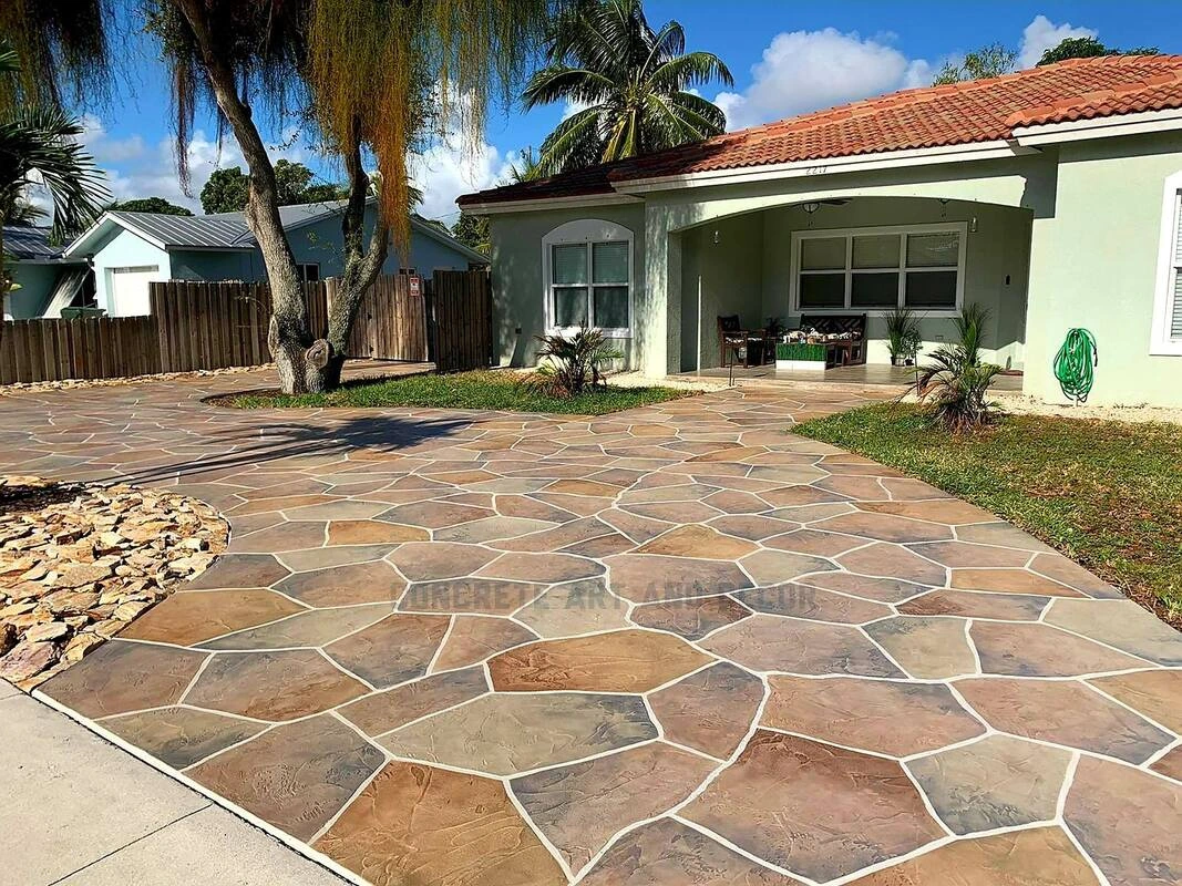 Custom stamped concrete in Lewisville TX featuring a warm-toned flagstone pattern driveway, perfectly complementing this Mediterranean-style home with tropical landscaping.