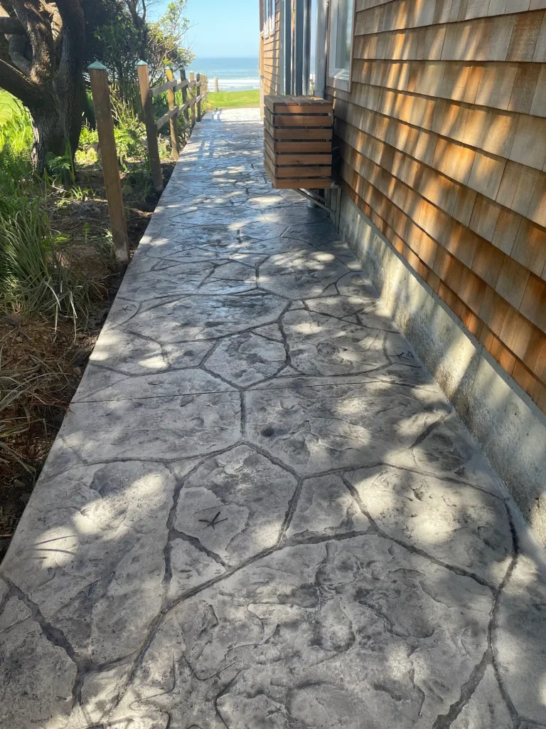 Coastal-inspired stamped concrete in Lewisville TX with natural stone pattern, creating an elegant walkway with ocean views and custom wooden fencing.